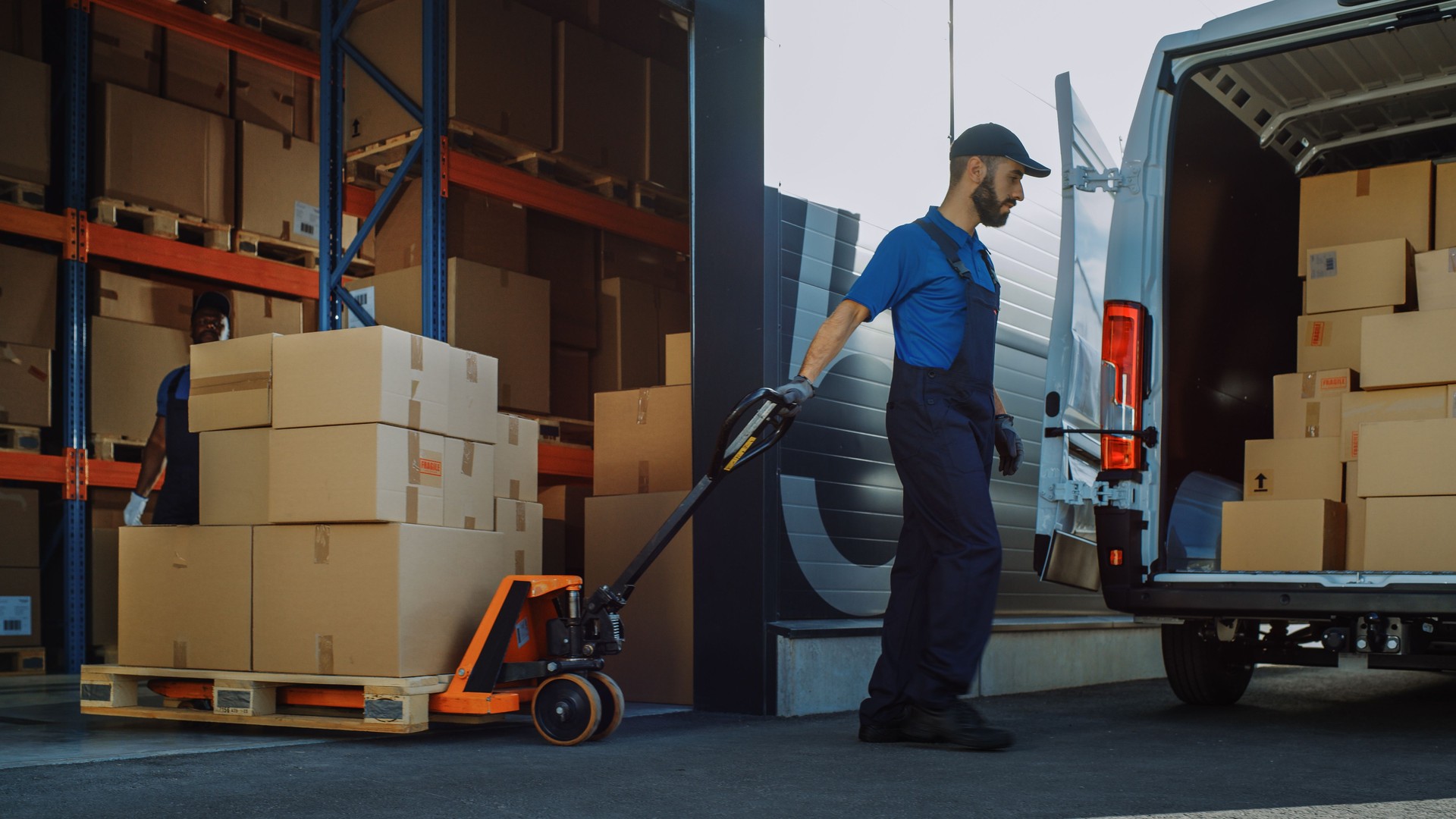 Outside of Logistics Distributions Warehouse: Diverse Team of Workers use Hand Pallet Truck Start Loading Delivery Truck with Cardboard Boxes, Online Orders, Purchases, E-Commerce Goods.