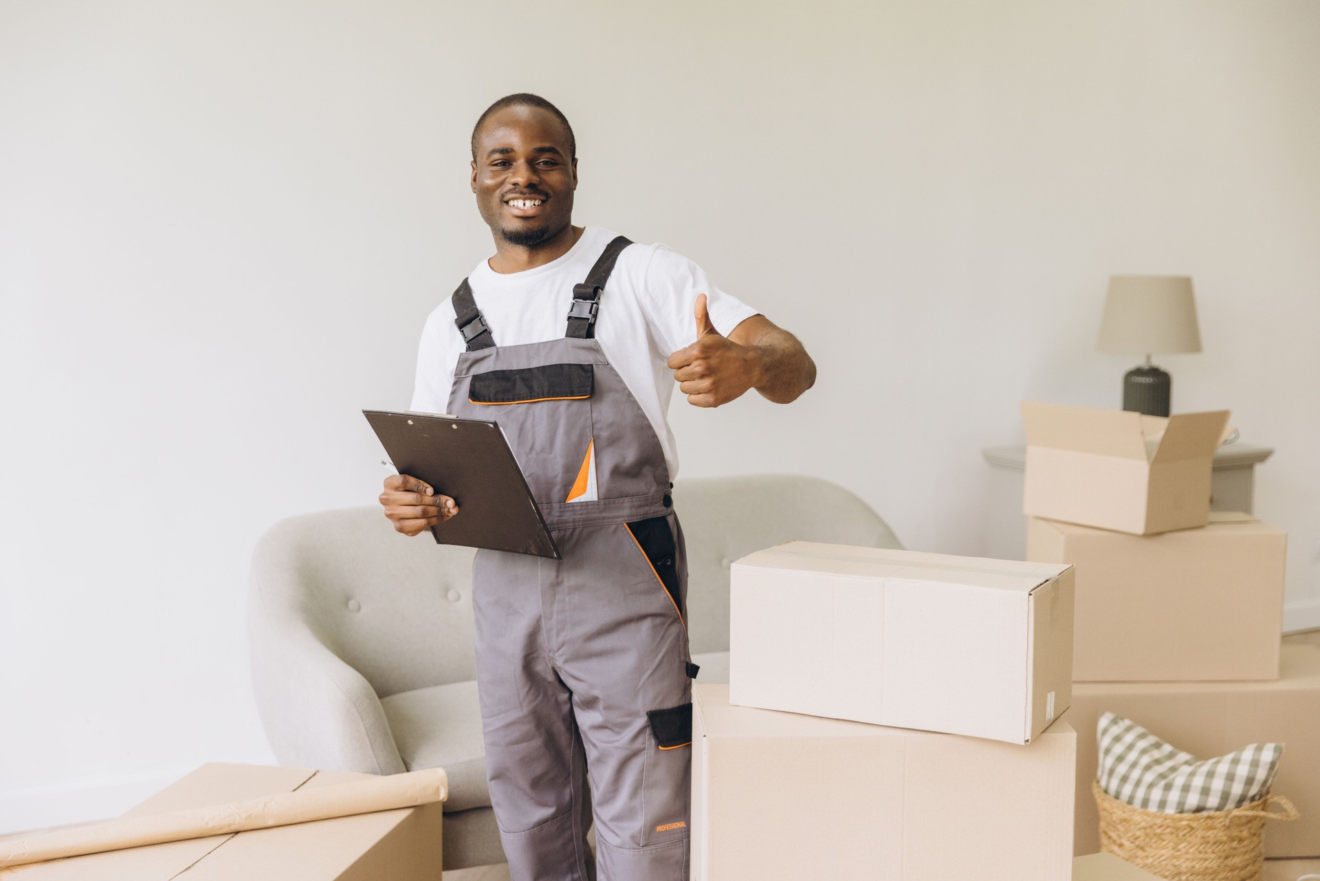 Smiling african american mover holding clipboard and showing thumbs up during relocation